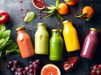 colourful smoothie drinks in glass bottles surrounded by fresh fruit 